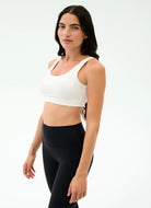 Woman wearing a white sports bra and black leggings on a white background