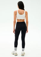 Person wearing a white sports bra and black leggings on a white background