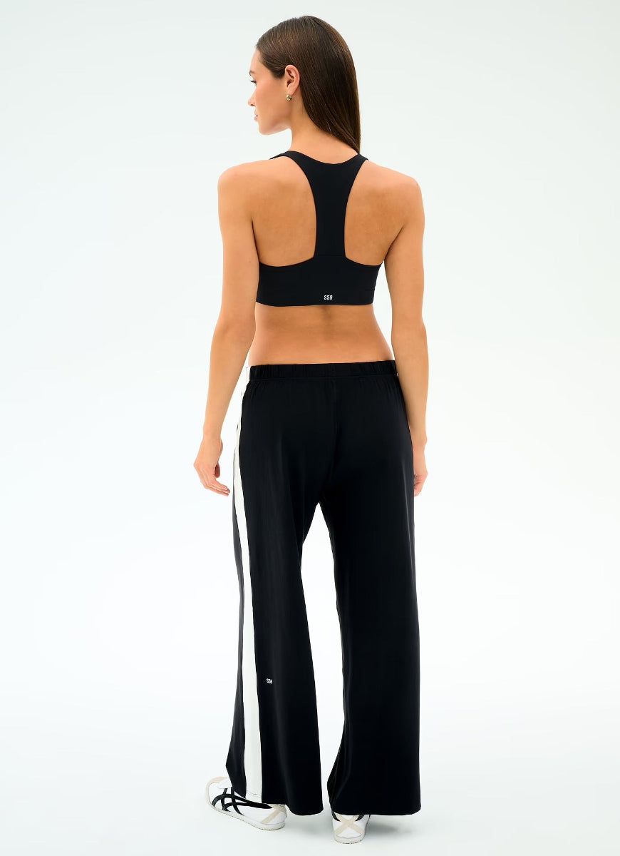 Woman wearing a black sports bra and black pants with white stripes on a white background