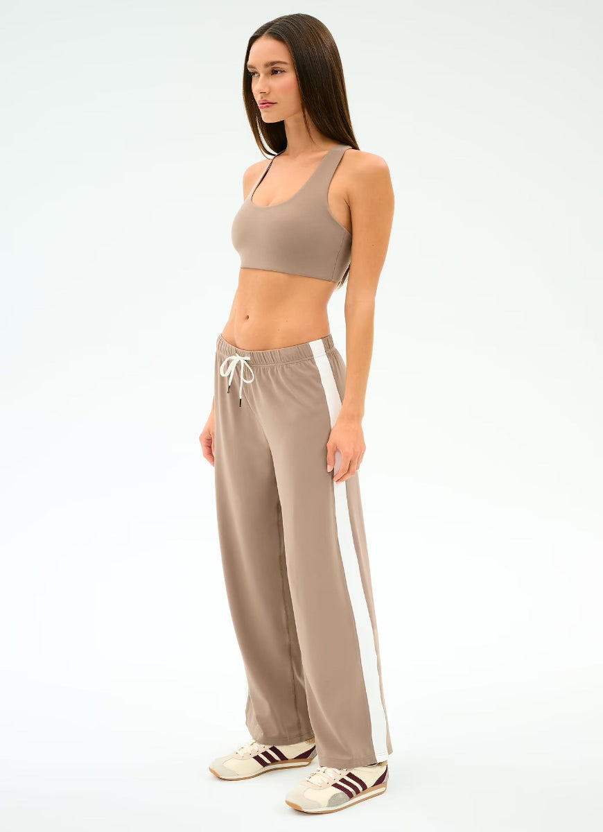 Woman wearing a beige sports bra and pants with white drawstrings on a white background