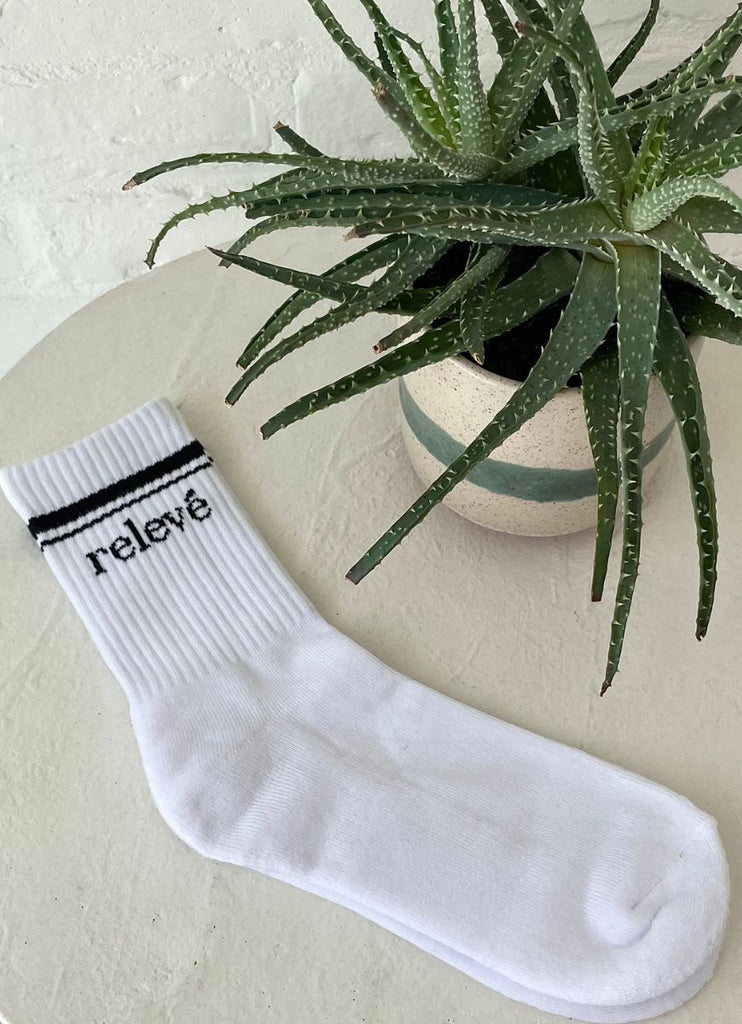 relevé Crew Socks in White with Black Logo Laying Flat on a Table