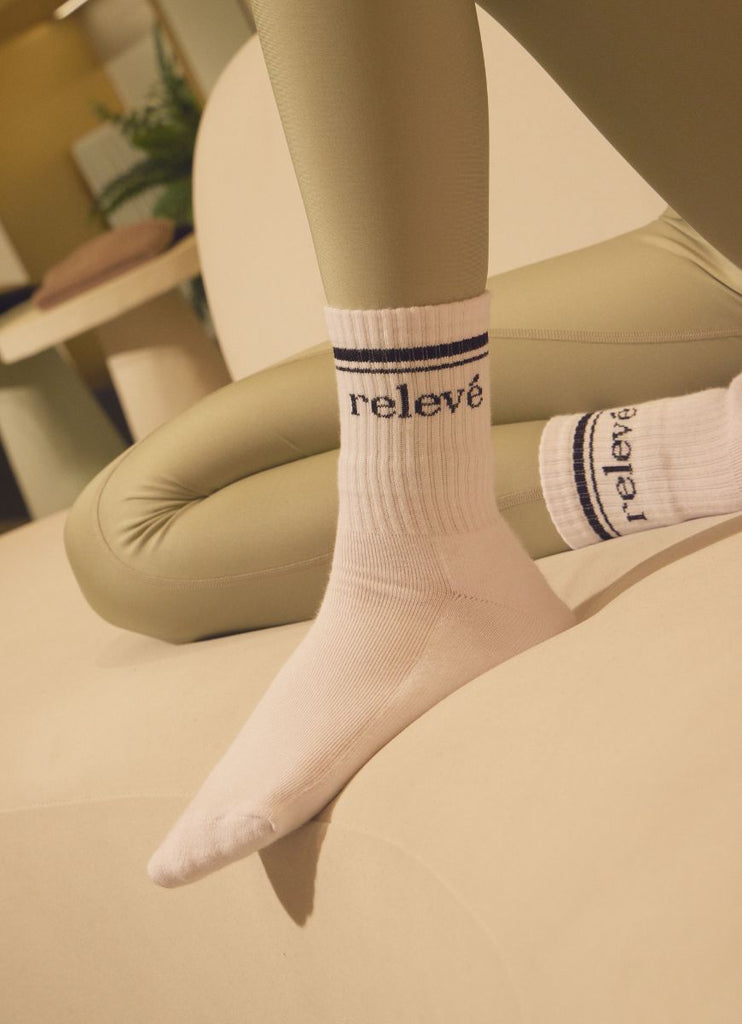 relevé Crew Socks in White with Black Logo Model Knee Bent on Sofa